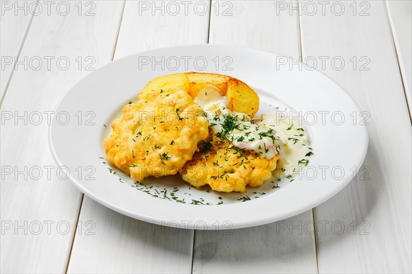 Ground chicken meat cutlet with fried potato wedges and creamy sauce with bacon on white wooden table