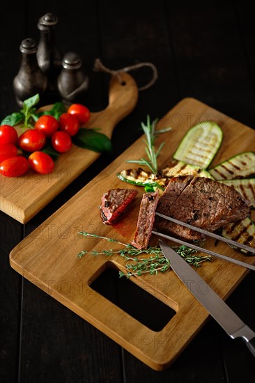 Low key photo of grilled beefsteak and zucchini on wooden cutting board