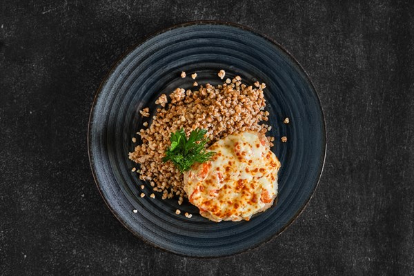 Top view of chopped pork meat baked with cheese and tomato served with buckwheat porridge