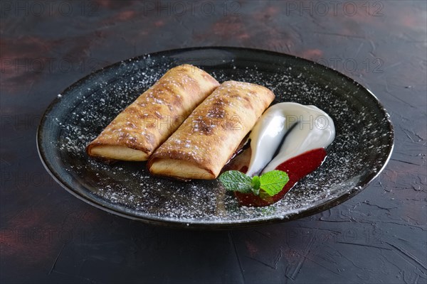 Sweet pancakes stuffed with curd and decorated with sour cream and strawberry jam