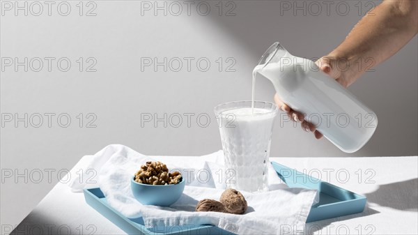 Person pouring milk full glass with walnuts tray