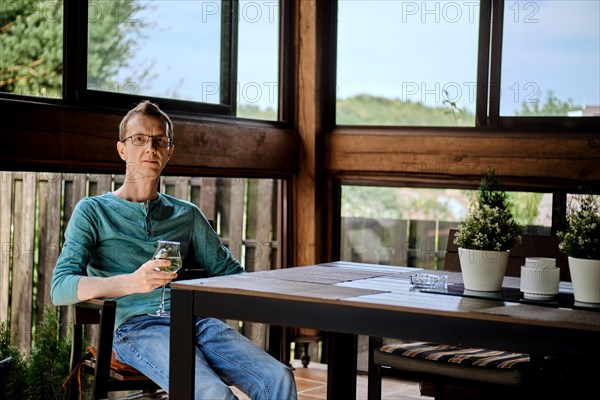 Middle aged man is resting on the veranda with a glass of wine