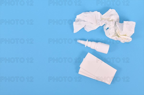 Top view of nasal spray bottle and used tissues used during common cold on blue background