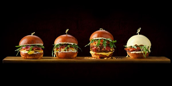 Set of four burgers with different types of meat on wooden serving board