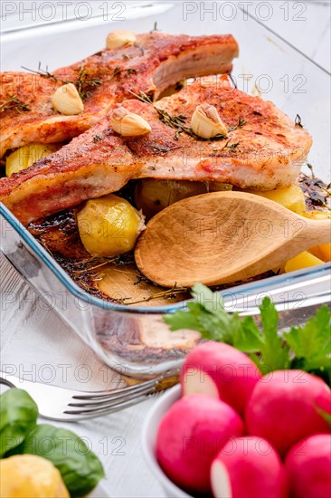 Steak with bone and potato baked in oven in a roasting pan with garlic and thyme