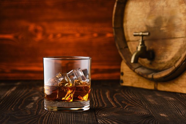 Glass of whisky with ice with barrel on background