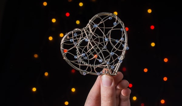 Heart shaped metal cage in hand on bokeh light background