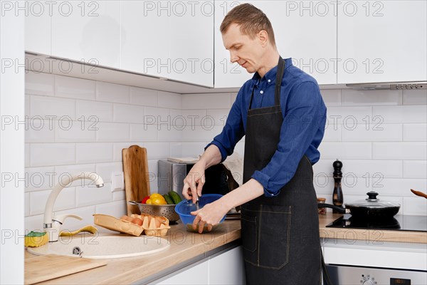 A middle aged man whips an egg with a whisk to make an omelet