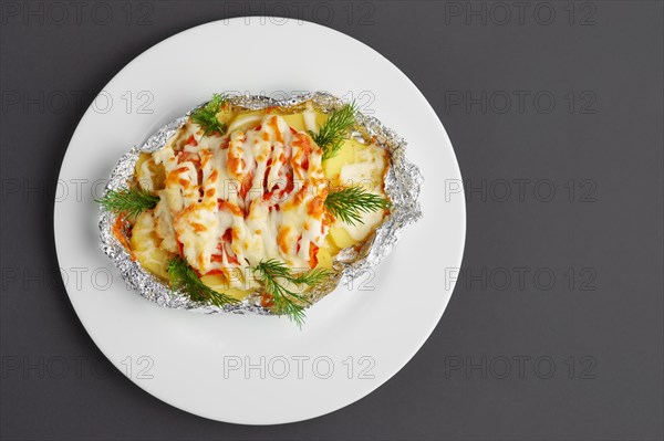 Top view of fried in foil sea fish and potato with paprika and cheese on gray background