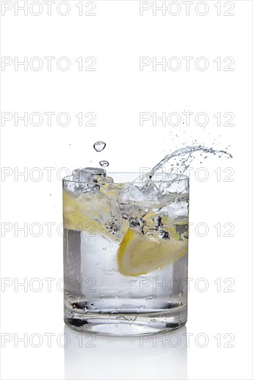 Ice cube and lemon splashing cocktail in oldfashioned glass. Drink with splashing citrus isolated on white