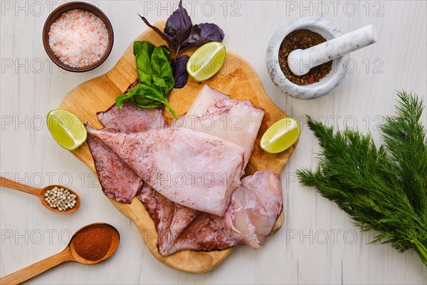 Top view of raw fresh unpeeled squid on wooden cutting board with spice and herbs