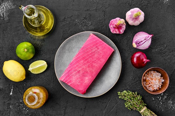 Top view of raw tuna fillet in plate with spice on black background