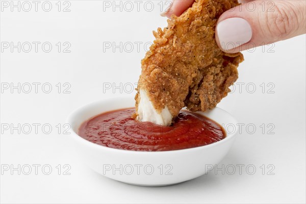 Front view hand dipping fried chicken ketchup
