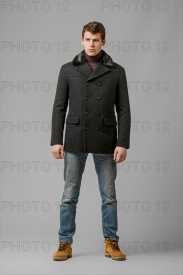 Full length portrait of handsome man in warm woolen coat posing in studio