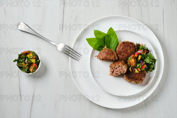 Top view of fried veal meatballs on a plate with basil and tomato