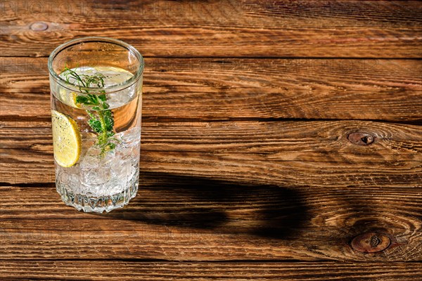 Carbonated cold water with ice and lemon dropping long shadow on wooden table