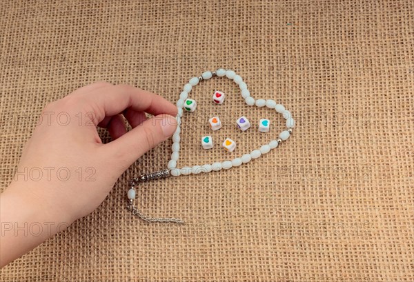 Heart shaped object in hand by a praying beads on canvas