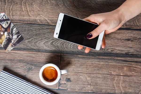 Top view of table with cup of coffee. Hand holding smartphone