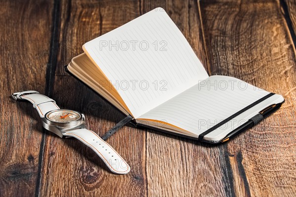 Open blank notebook with pen and wrist watch on wooden table