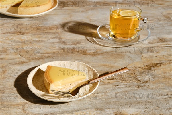 Piece of lemon tart with tea under direct sunlight with hard shadows on the table