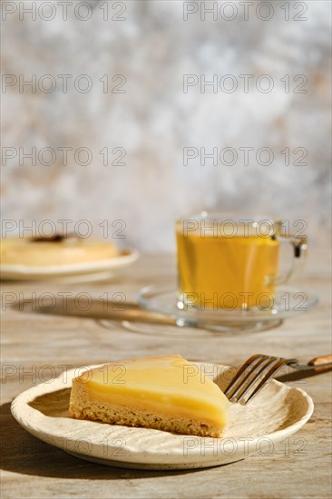 Piece of lemon tart with tea under direct sunlight with hard shadows on the table