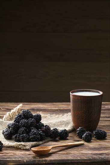 Heap of fresh dewberry on sackcloth table-napkin and clay cup with milk on wooden table