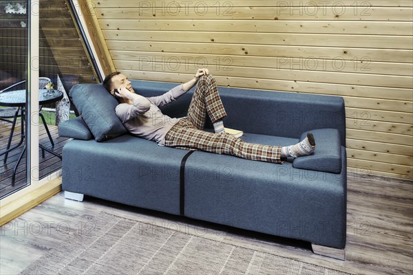 Middle aged man talking on the smartphone while resting in his forest cabin on vacations