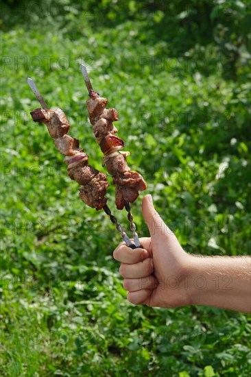 Hand with thumb up holding skewer with shashlik