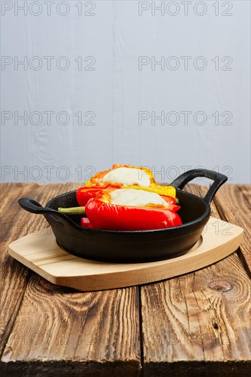 Bell pepper stuffed with meat with melted cheese mozzarella on top baked in oven in cast iron skillet. Top view. Natural wooden background