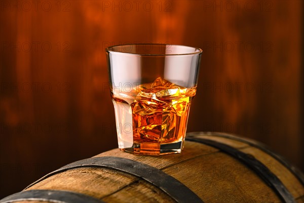 Glass of whisky with ice on the top of barrel