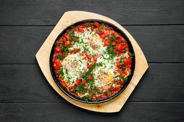 Overhead view of eggs fried with ham and tomato in cast iron skillet