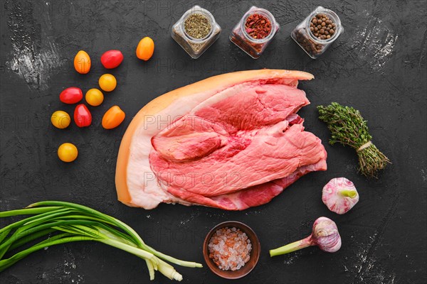 Raw fresh pork shoulder joint meat with spice and herbs on black background