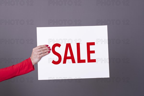 Female hand holding a Sale poster. Studio shot