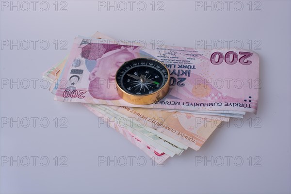 Turkish Lira banknotes by the side of a compass on white background
