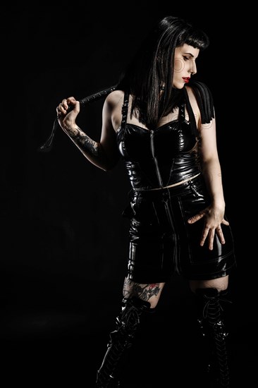 Woman with black hair and tattos in vinyl and latex outfit and whip