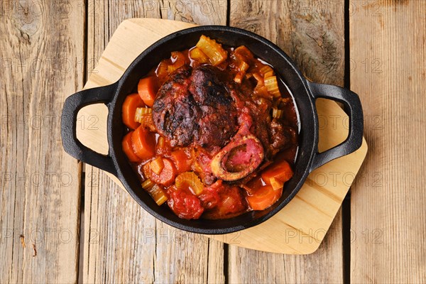 Overhead view of cast iron skillet with ossobuco on wooden table