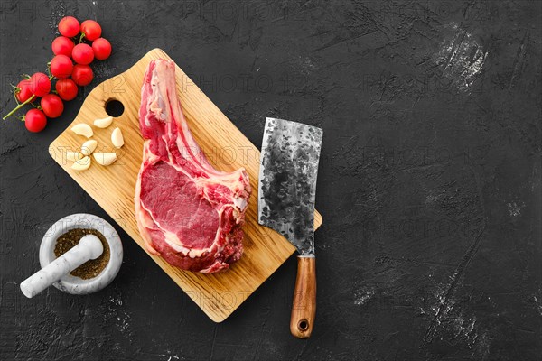 Top view of beef ribeye steak bone-in with spice on black background