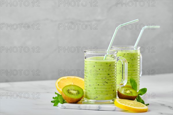 Two glasses with kiwi and lemon smoothie with mint on marble background and slices of fruits