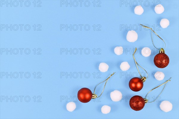 Christmas flat lay with red tree ornament baubles and white fluffy snowballs on light blue background with empty copy space