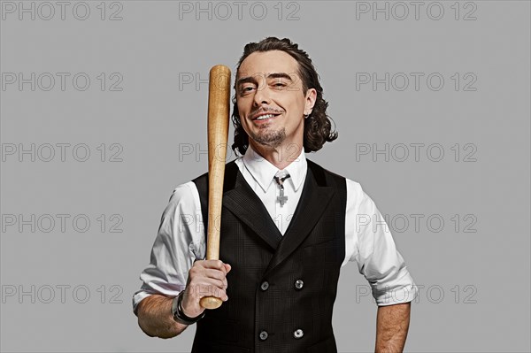 Dramatic man in white shirt and black vest with long curly hair holding baseball bat