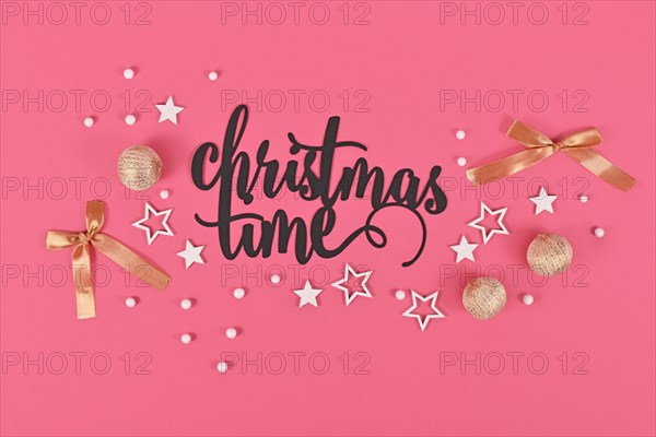 Black 'Christmas time' text next to golden and white bauble and star ornaments on pink background