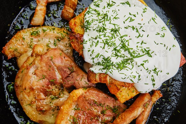 Close up view of potato casserole with fried pork mini belly slices on dark wooden table