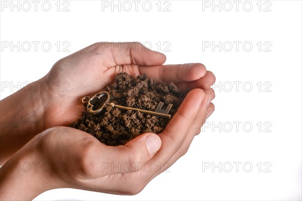 Golden key in handful soil in hand on an isolated background