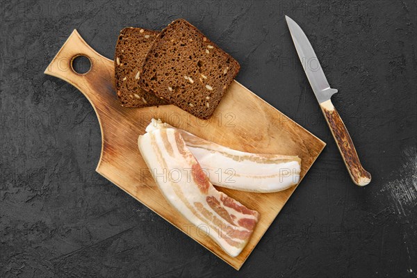 Top view of two slices of bacon and brown bread on wooden cutting board