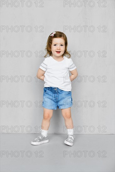 Two years old girl in white t-short and jeans shorts posing in studio