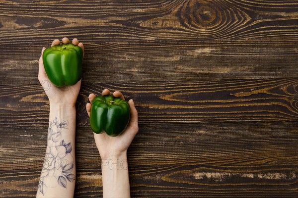 Overhead view of fresh green bell pepper in hands over wooden background