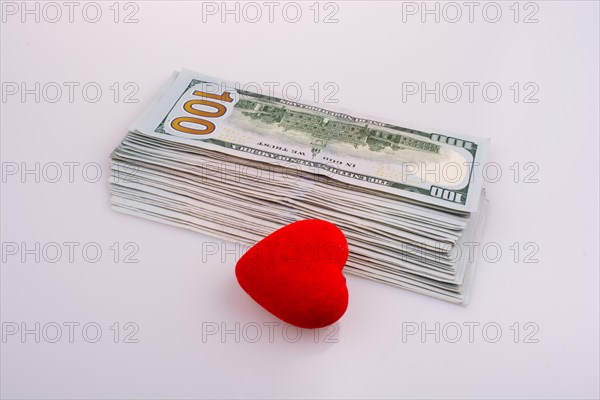 American dollar banknotes by the side of a red color heart shaped object on white background