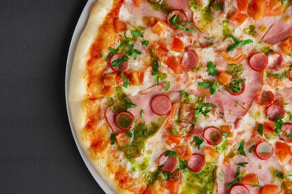 Top view of pizza with ham and sausage decorated with bell pepper and parsley