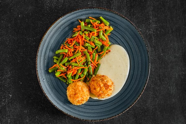 Top view of meatballs in breading served with green bean and spicy carrot