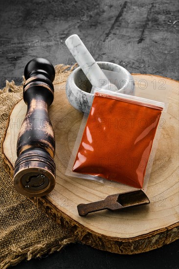 Wooden cross section with smoked paprika in plastic package and stone mortar and mill